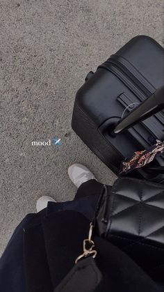 a black suitcase sitting on the ground next to a person's feet and handbag