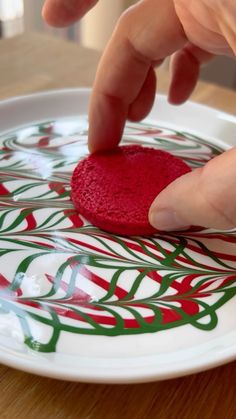 a person is touching a red heart on a white plate with green and red designs