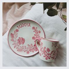 a pink and white plate with a cup on it sitting next to a napkin that says mama