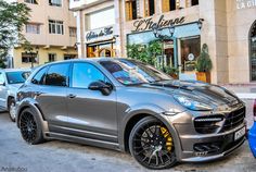 a grey porsche cayen is parked in front of a building with two blue cars