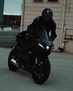 a man riding on the back of a black motorcycle in front of a white building