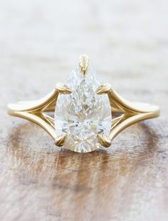 a yellow gold ring with a pear shaped diamond in the center on a wooden surface