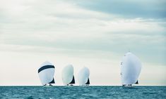 three sailboats in the ocean on a cloudy day