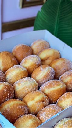 a box filled with sugar covered donuts sitting on top of a wooden table next to a green leaf