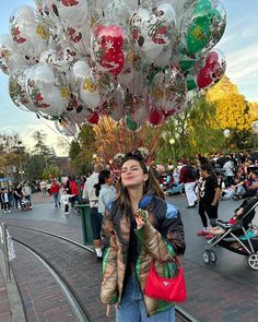 a woman standing next to a bunch of balloons on top of a street near people