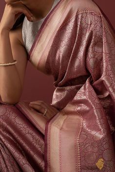 a woman in a pink sari sitting on the ground with her hand under her chin