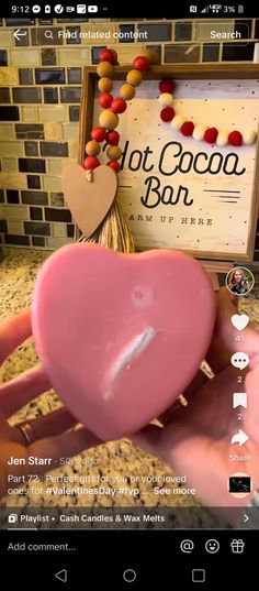 someone holding a pink heart in front of a sign that says hot cocoa bar on it