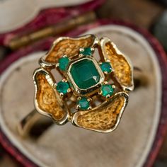 This beautiful circa 1970s ring is crafted of 18k yellow gold and features emerald cut emerald in the center surround by round cut emeralds. The ring is currently a size 10. Art Deco Green Emerald Ring In 14k Gold, Art Deco Emerald Ring In 14k Gold, Formal Yellow Gold Cluster Ring With Emerald, Classic Gold Emerald Cluster Ring, Yellow Gold Cluster Ring For May Birthstone, Emerald Cut, 14k Gold Emerald Cut Art Deco Ring, Green Emerald Cut 14k Gold Cluster Ring, Emerald Cut Green Cluster Ring In 14k Gold, Emerald Cut Yellow Gold Cluster Ring For May Birthstone