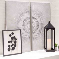 two framed art pieces sitting on top of a white shelf next to a candle holder