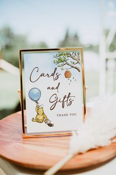 a winnie the pooh card and gift box on a wooden table with white feathers