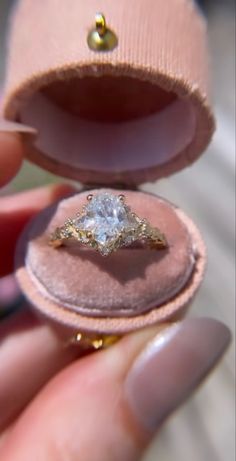 a woman's hand holding an open ring box with a diamond in the middle