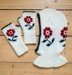 two white gloves with red flowers on them sitting on a wooden floor next to each other