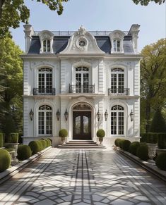 a large white house with lots of windows and bushes in front of the entrance to it