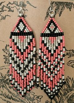 pink, black and white beaded earrings hanging from a hook on a brown background