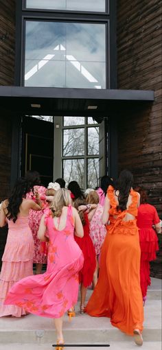 a group of women in long dresses are walking out of a building with their arms around each other