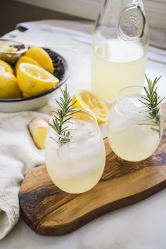 two glasses with lemonade and rosemary garnish sit on a wooden cutting board