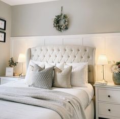 a white bed topped with lots of pillows next to two lamps and a clock on the wall