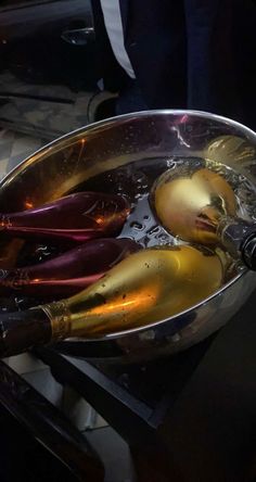 champagne being poured into a metal bowl on top of a table with wine bottles in it