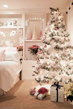 a white christmas tree in a bedroom decorated with lights and presents next to the bed