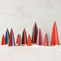 a row of colorful paper trees sitting on top of a snow covered ground in front of a white wall