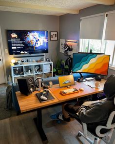 a desk with two monitors and speakers in front of a television on top of a wooden table