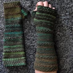 a person's hand is holding onto a pair of knitted fingerless mitts