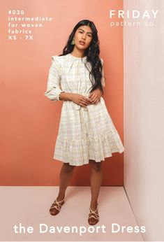 a woman standing in front of a pink wall wearing a white dress and brown sandals