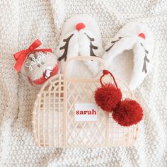 a pair of white slippers with red pom - poms are on the bed