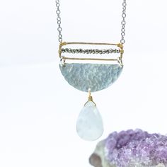 Embrace the enchanting allure of our Moonstone Radiance Necklace, a harmonious blend of celestial elegance and artistic craftsmanship. At its heart, a large moonstone, glowing with an ethereal light, gracefully hangs from a textured silver half circle, capturing the essence of lunar mystique. Above, a delicate gold rectangle, meticulously adorned with tiny sparkling pyrite gemstones, stretches the length of the disc, adding a touch of subtle brilliance to the design. The interplay of textures an White Moon Shaped Mystical Necklace, Mystical Moon Shaped White Necklace, Mystical White Moon-shaped Necklace, Mystical White Moon Necklace, Artisan Silver Necklace With Moon Phase Detail, Artisan Silver Necklace With Moon Phase, Artisan Silver Necklace With Moon Charm, Unique Crescent Shaped White Jewelry, Unique White Crescent Jewelry