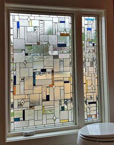 a toilet sitting next to a window covered in lots of different colored glass tiles on the wall