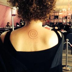 the back of a woman's neck with a spiral tattoo on her left shoulder