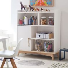 a white book shelf filled with lots of toys next to a table and chair in a room