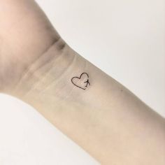 a small heart tattoo on the wrist is shown in black ink, with an arrow at the center