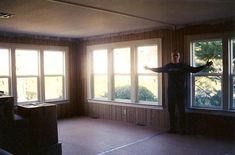 a man standing in an empty room with his arms out to the side and windows open