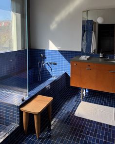 a blue tiled bathroom with a wooden stool in the corner and a shower stall next to it