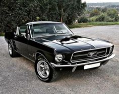 an old ford mustang sitting in the middle of a parking lot next to some trees