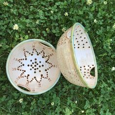 two ceramic bowls sitting on top of green grass next to eachother with holes in them