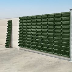 several green bins are lined up on the side of a building with white walls