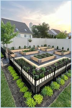 an outdoor garden area with raised beds and plants in the center, surrounded by white picket fence