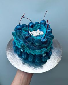 a hand holding a cake with blue icing and decorations on the top, in front of a gray background