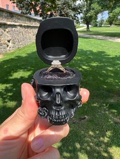 a hand holding up a black skull ring box