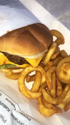 a cheeseburger and onion rings are sitting on a paper wrapper, ready to be eaten