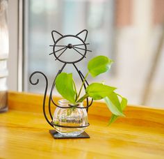 a plant in a glass vase with a metal cat figure on the table next to it