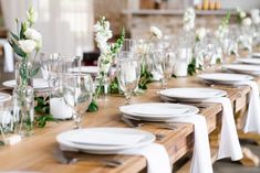 the table is set with white and green flowers in vases on each place setting