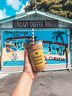 a person holding up a cup of coffee in front of a sign for the cuban coffee queen