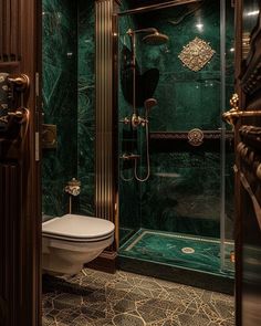 a bathroom with green marble walls and flooring is pictured in this image, there is a toilet and shower stall