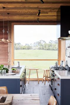 an open kitchen with wooden walls and flooring next to a large window that looks out onto a field