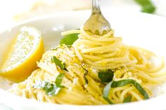 a fork full of spaghetti with basil and lemon wedges on the side in a white bowl