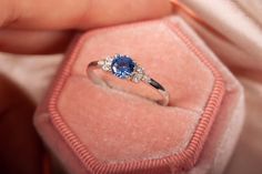 a close up of a person's hand holding a ring in a velvet box