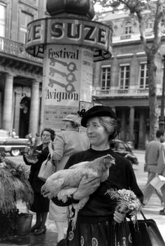 an old photo of a woman holding chickens in her hands while walking down the street